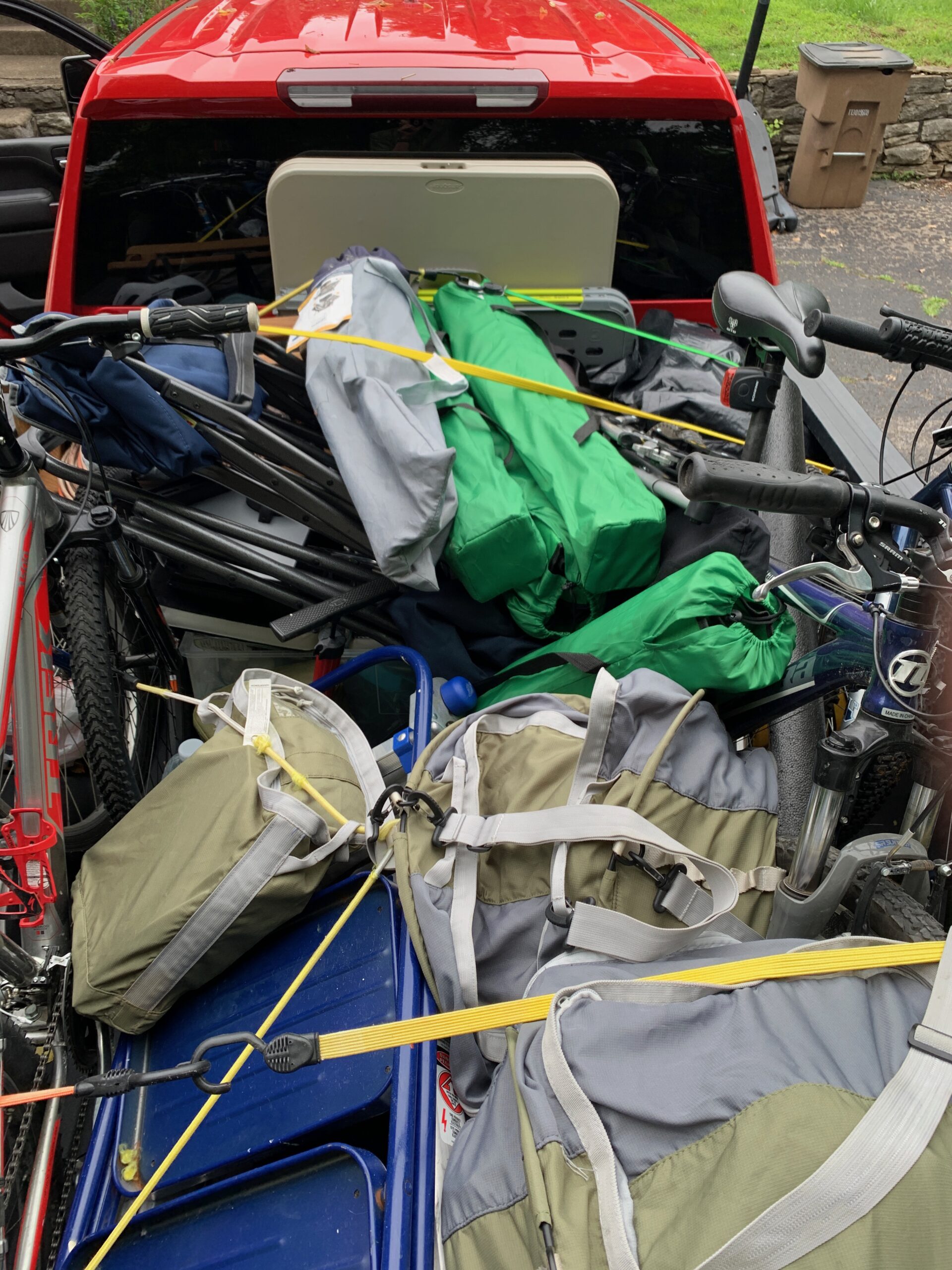 2025 FCF 02 — Parcked Truck The bed of a pickup truck loaded with camping gear, including bagged camping chairs, and bicycles. It is very full and tied down with bungee cords.