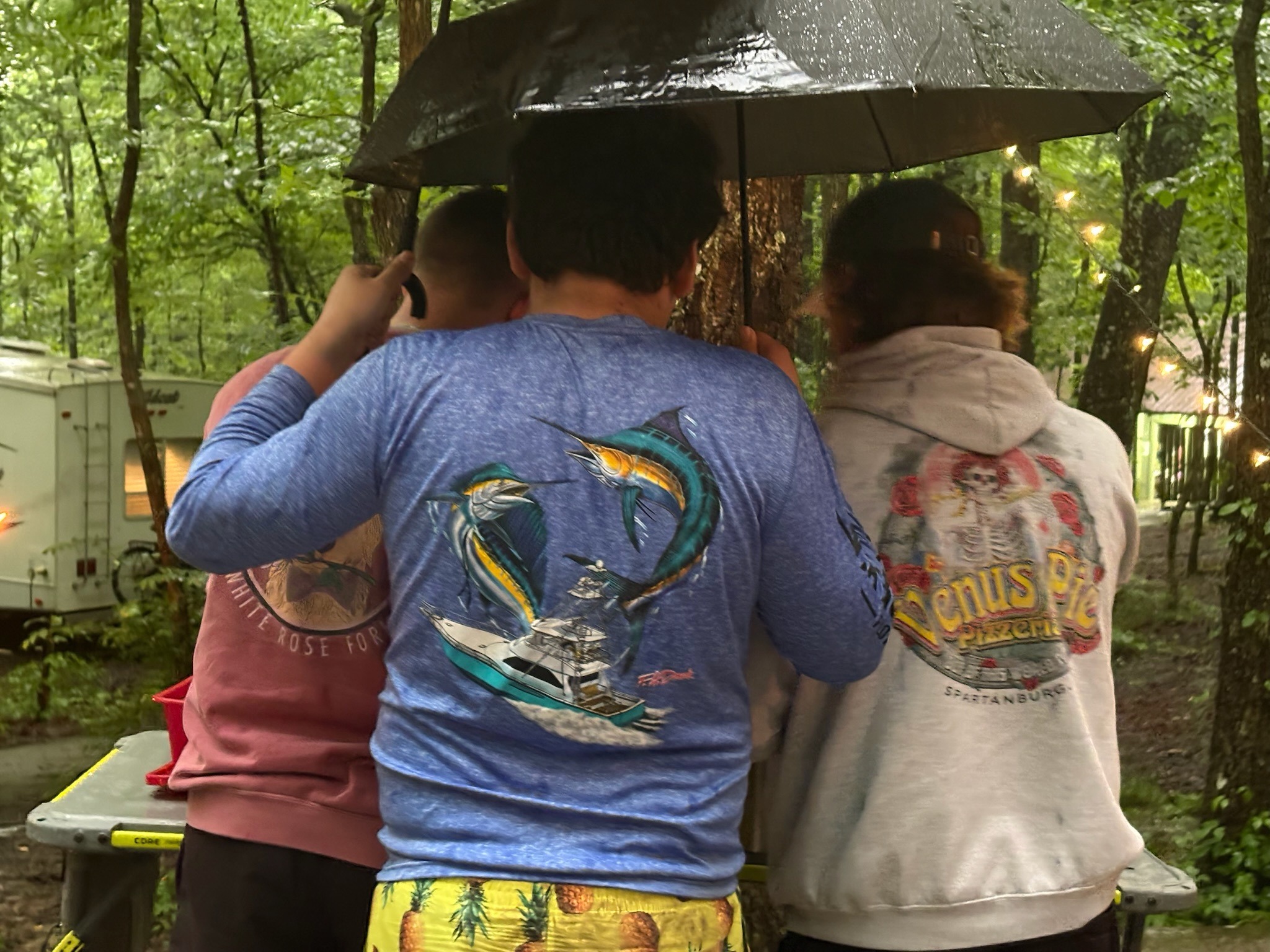 2025 FCF Lara 10 The backs of three boys. One is holding two umbrellas.