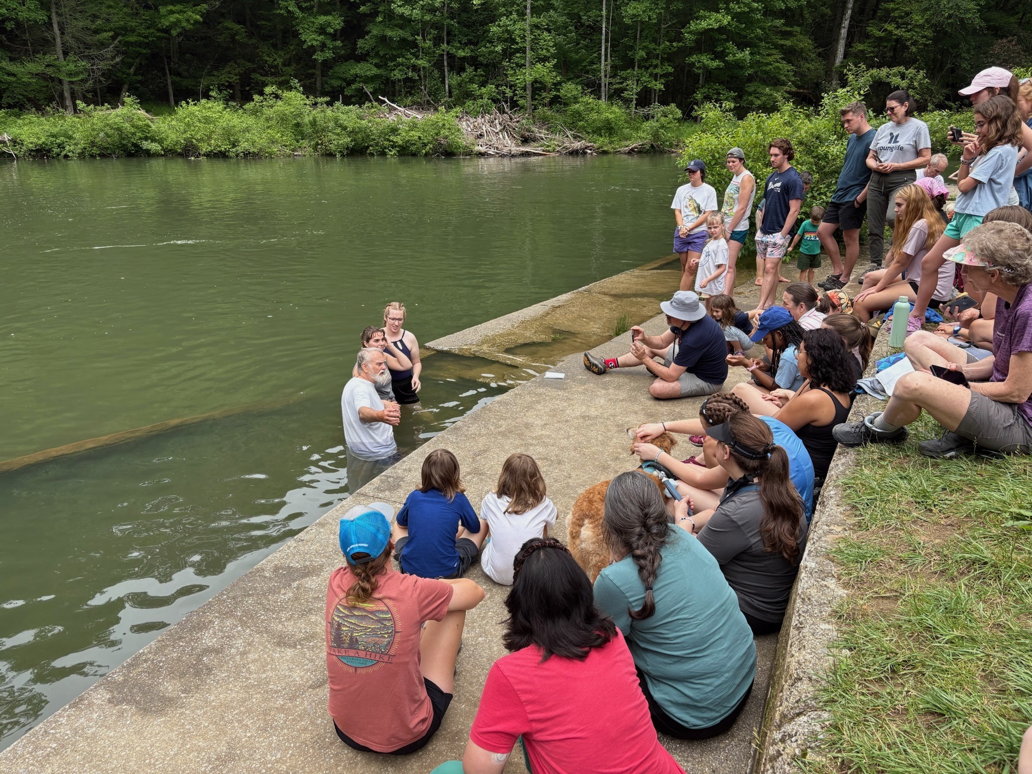 2025 FCF Lara 15 Three people are standing in waist-high water in preparation for baptism. The rest of us are sitting around watching.